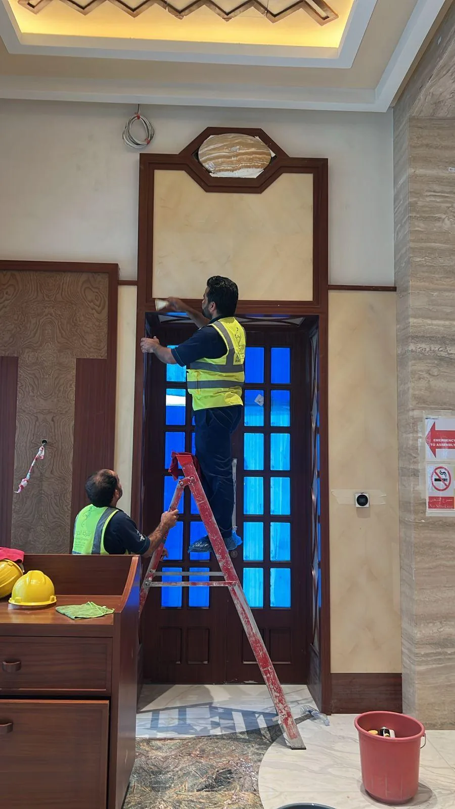 عمال يستخدمون سلمًا لتنظيف أعلى مدخل وتفاصيل باب مرتفع